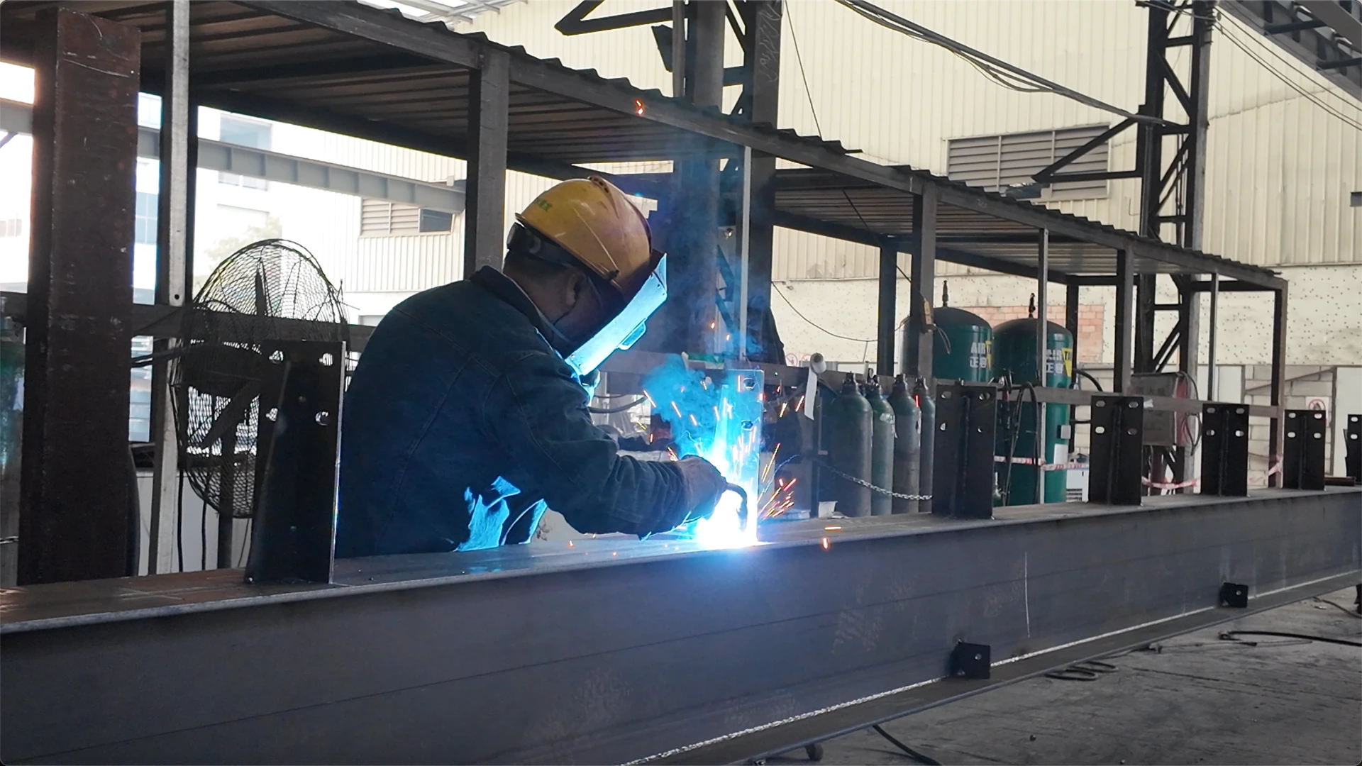 Worker welding an H-beam component in a steel fabrication workshop